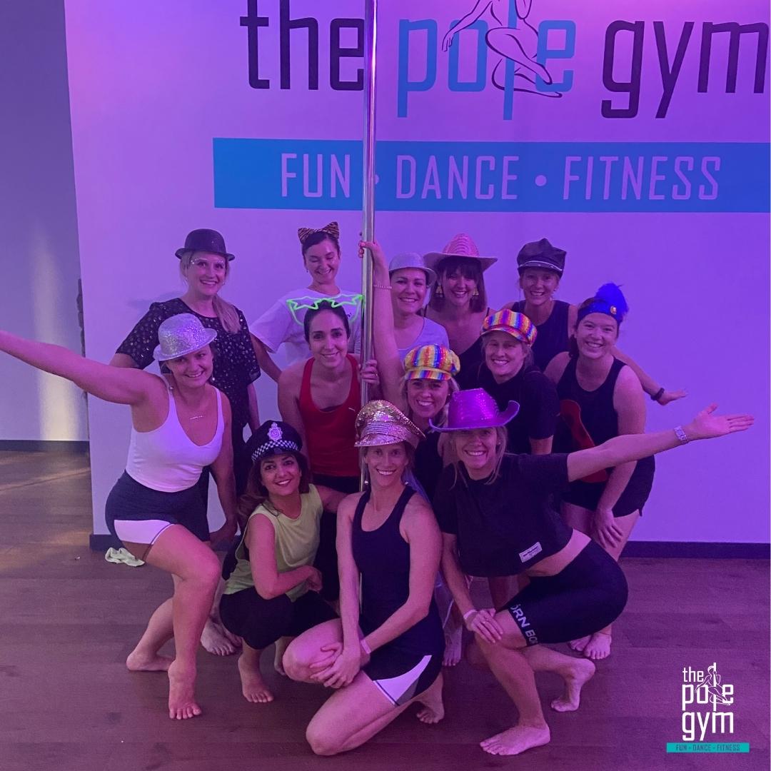 A group of women wearing fun accessories and pole dancing in a Deluxe Pole Party at The Pole Gym Brisbane City.